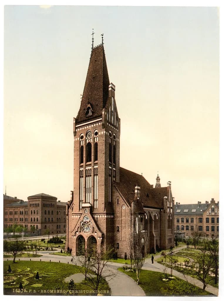 A historic photochrom of the brick Bromberg Christuskirche with a tall, pointed spire, surrounded by green lawns and other buildings under a clear sky.